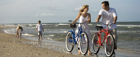 Padre y madre recorren con bicicleta en mano la playa junto a sus hijos