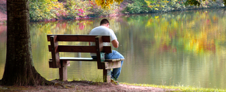 joven sentado en una banca, en medio de un jardín botánico