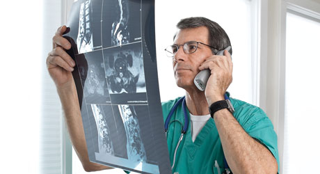 Doctor revisa una radiografía de un paciente mientras habla por teléfono con él