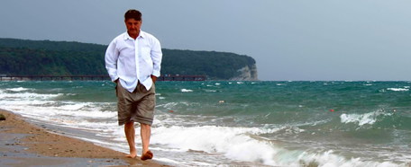 Hombre maduro con camisa  blanca recorre la costa marina