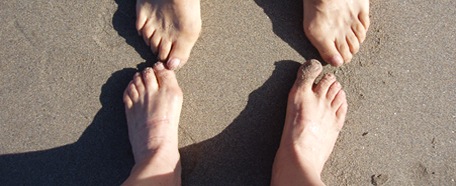 dos pares de pies, uno en frente del otro, sobre la arena húmeda de la playa