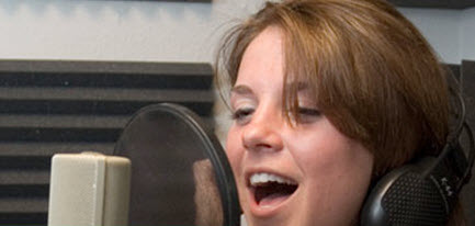 Una cantante, con audífonos y micrófono de estudio, graba una canción