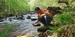 Hombre toma agua de un río natural