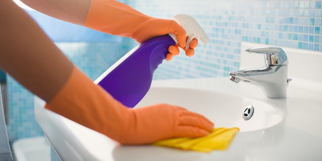 Persona limpiando lavamanos con guantes y paño