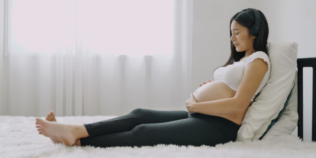 Mujer embarazada en cama con audífonos