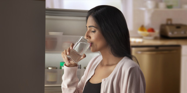 Mujer toma vaso de agua cerca de su refrigerador